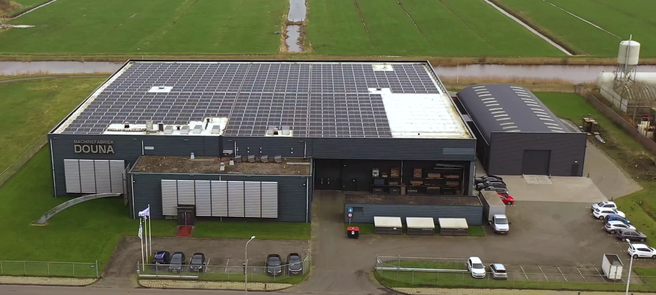Luchtfoto van het Douna-bedrijfspand met zonnepanelen en omliggend landschap