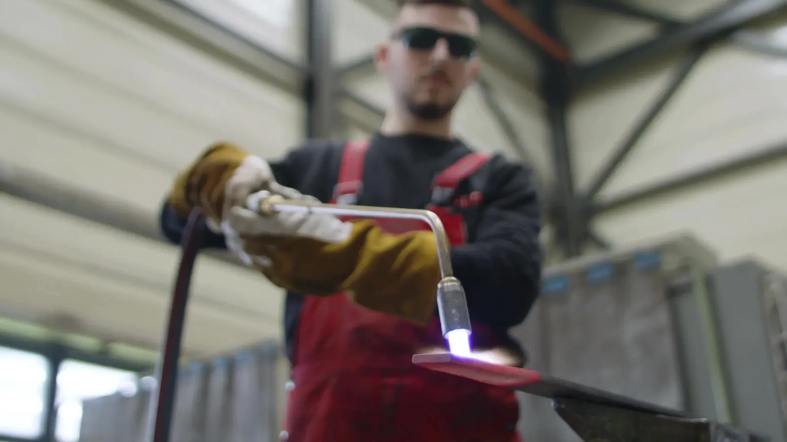 Ein Metallbearbeiter erhitzt ein Metallwerkstück mit einem Brenner in der Produktionshalle