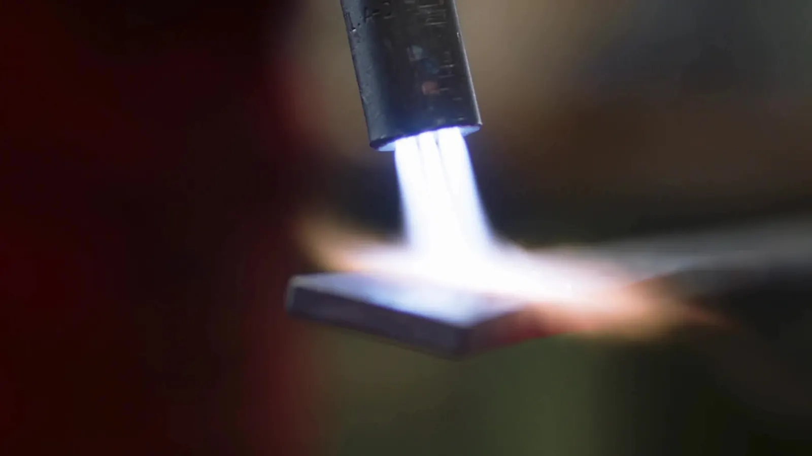 A blue torch flame heats the surface of a metal workpiece