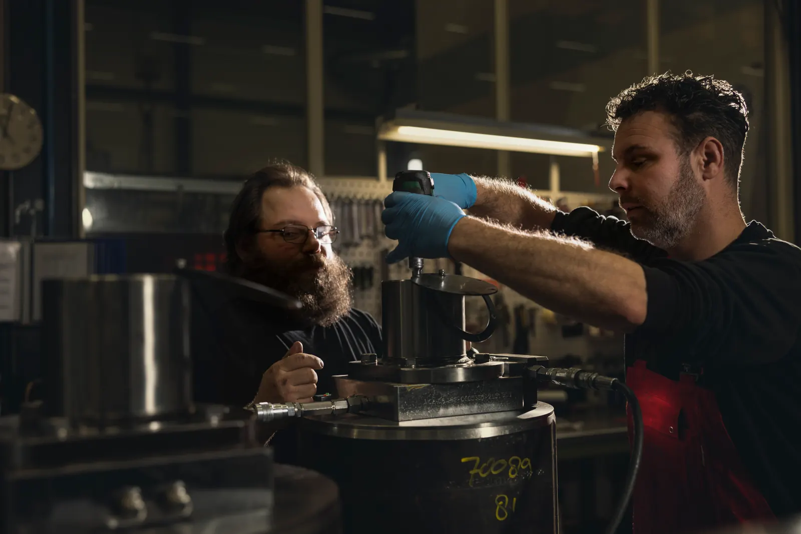 Zwei Mitarbeiter montieren gemeinsam ein zylindrisches Bauteil an einer mechanischen Baugruppe